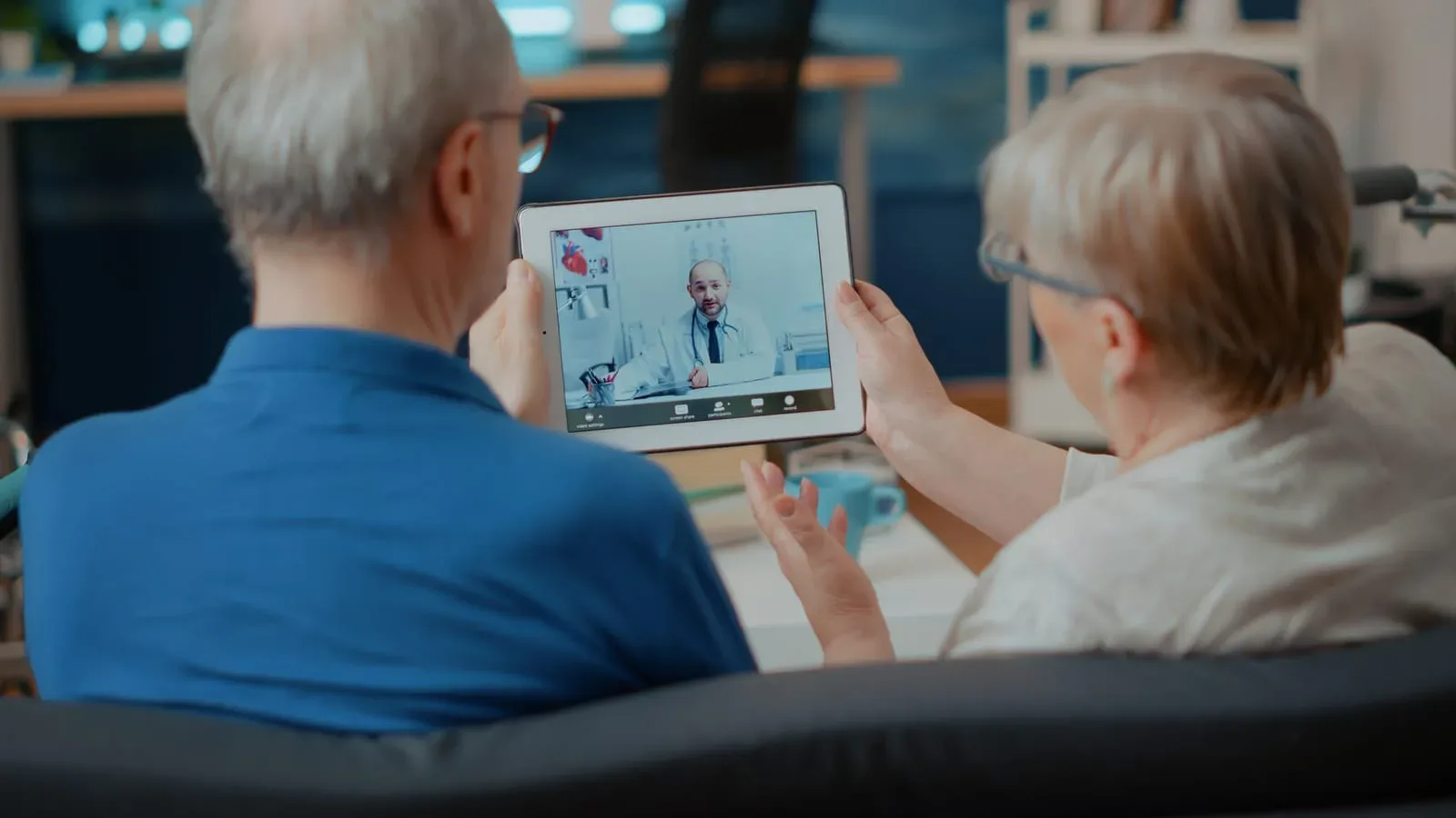 An older couple at home on a video visit with a doctor shown on a tablet