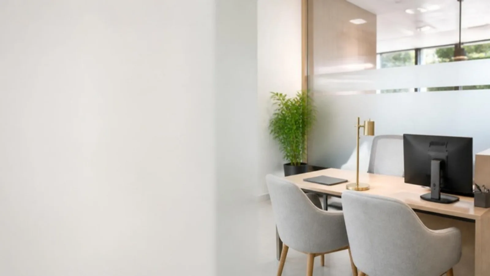 Bright, empty relationship manager office in a bank branch, with a wooden desk, a monitor, a brass desk lamp and two grey visitor chairs
