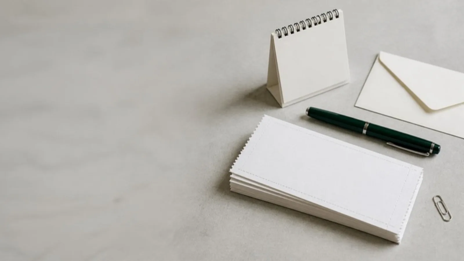 Overhead view of a stack of blank payment coupons, a desk calendar and a closed fountain pen on a pale grey stone desk