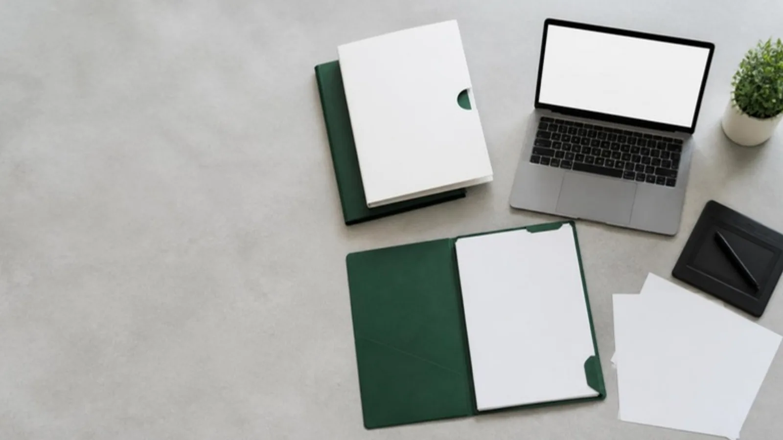 Overhead view of white and green trial document folders, a laptop and a signature pad on a pale grey desk