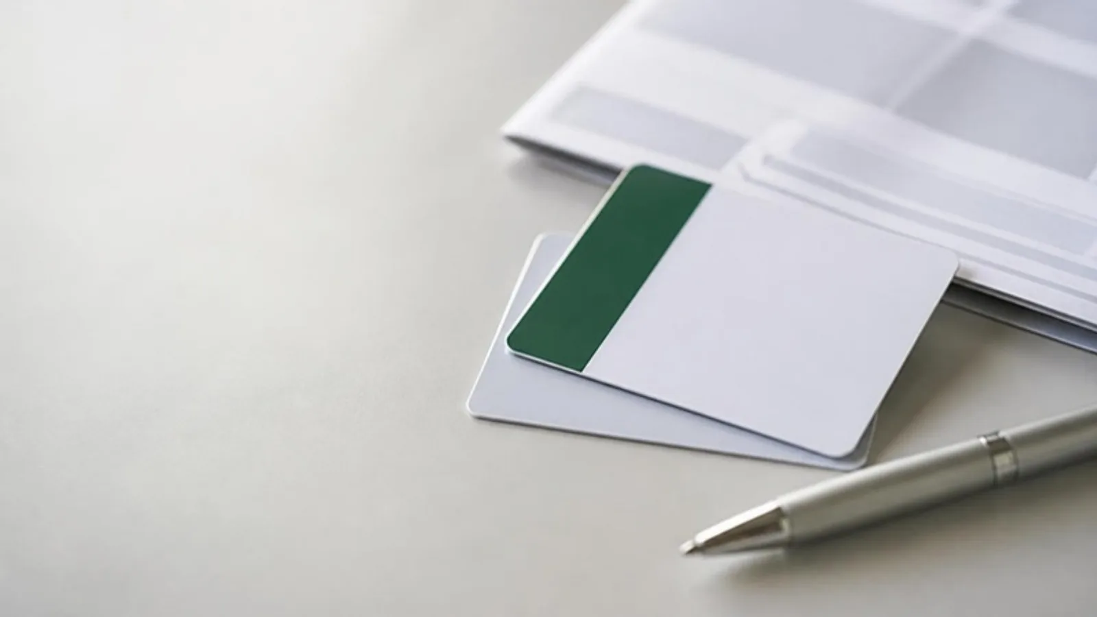 Two blank white member cards, one with a deep green band, overlapping beside a silver pen and a folded printed sheet on a pale grey desk