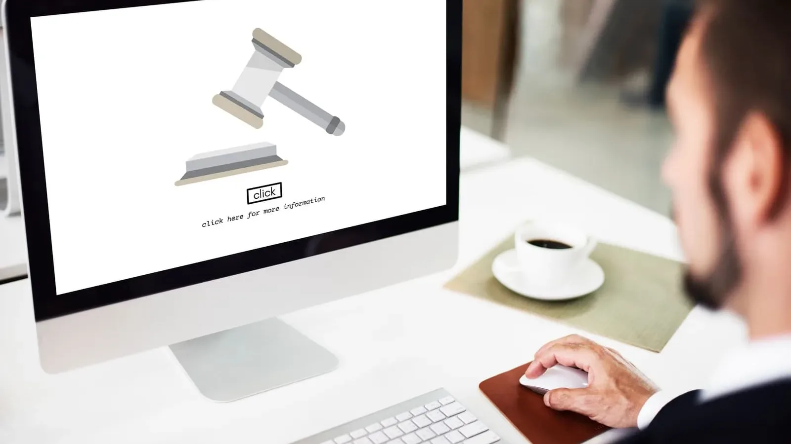 A lawyer at a desktop computer showing a gavel on screen, with a cup of coffee on the desk