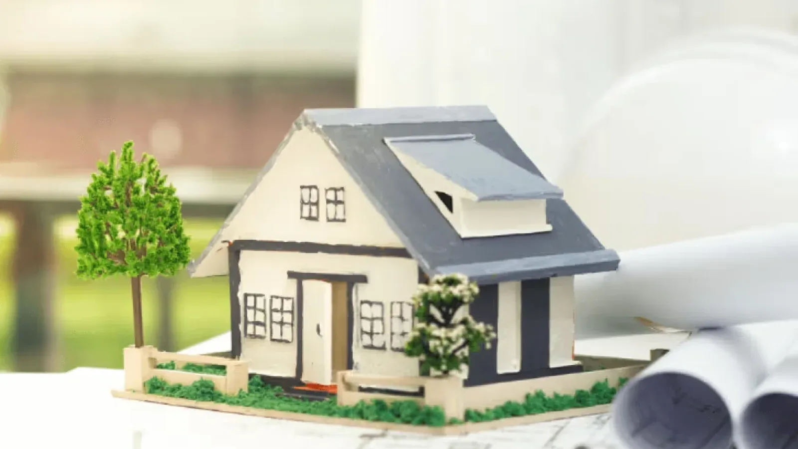 A small model house with a tree on rolled architectural blueprints on a white table